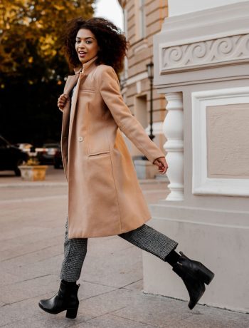 A full-length image of an elegant black woman in a luxurious beige coat and velvet sweater, showcasing a “budget fashion” style.