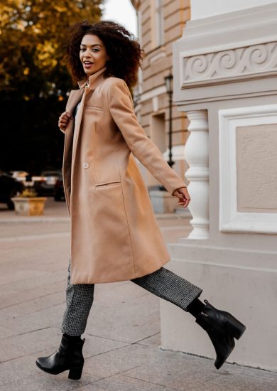 A full-length image of an elegant black woman in a luxurious beige coat and velvet sweater, showcasing a “budget fashion” style.