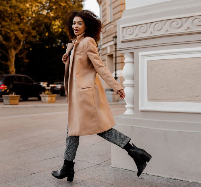 A full-length image of an elegant black woman in a luxurious beige coat and velvet sweater, showcasing a “budget fashion” style.