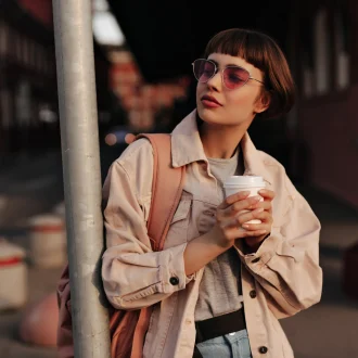 Woman in a Fall to Winter Minimalist Wardrobe, looking stylish in a tight outfit, holding a cup of tea in the city.