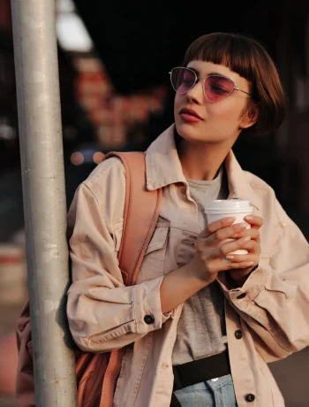 Woman in a Fall to Winter Minimalist Wardrobe, looking stylish in a tight outfit, holding a cup of tea in the city.