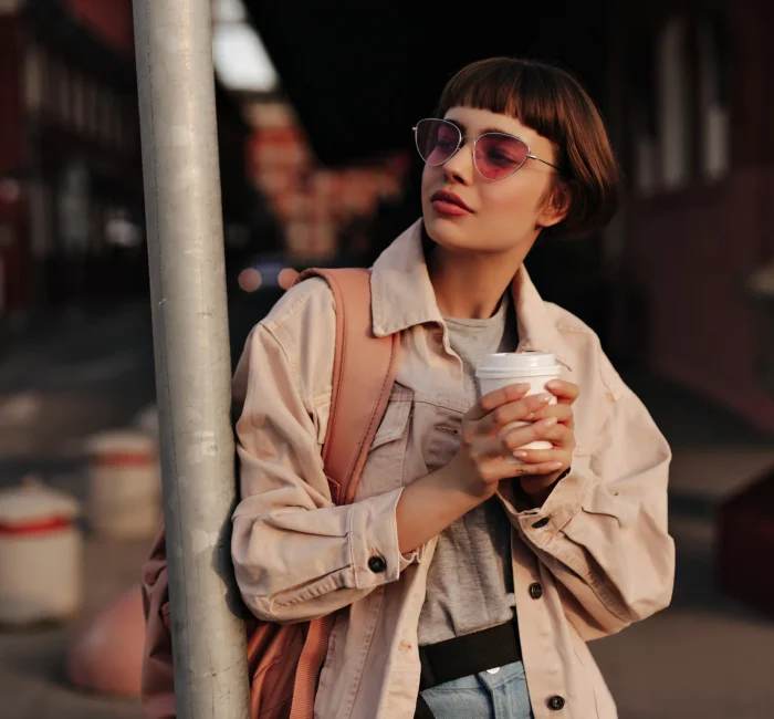 Woman in a Fall to Winter Minimalist Wardrobe, looking stylish in a tight outfit, holding a cup of tea in the city.