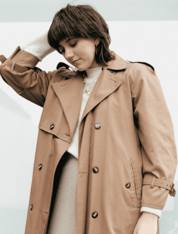 A stylish young woman on the street is seen touching her hair while layering clothes.