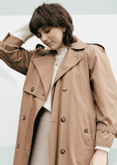 A stylish young woman on the street is seen touching her hair while layering clothes.