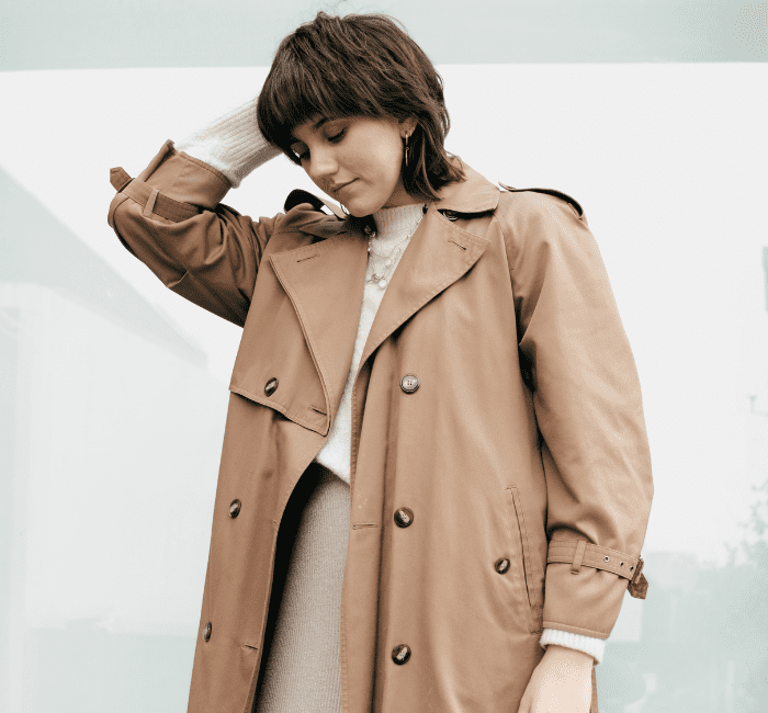 A stylish young woman on the street is seen touching her hair while layering clothes.