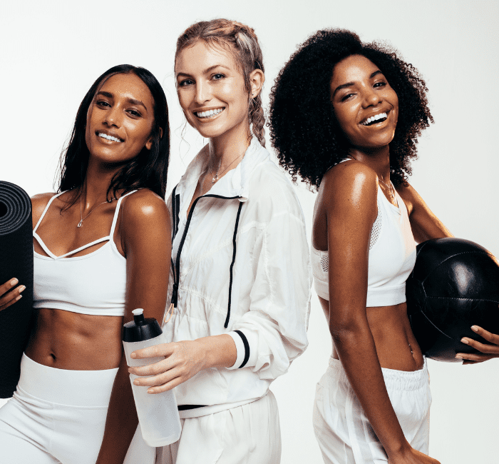 Women taking break after workout session in studio. Group of females in sportswear with exercise mat, water bottle and medicine ball on white background in their workout capsule wardrobe.