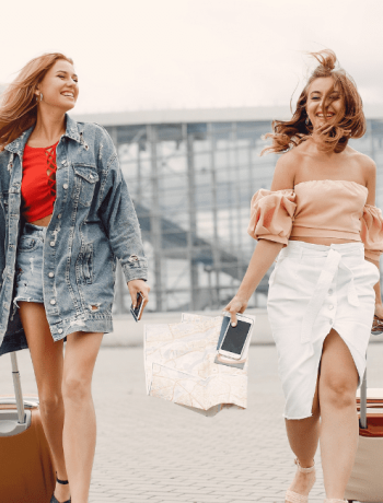 Two beautiful girls standing by the airport, showcasing their skill in traveling light